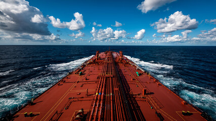 A super tanker is proceeding by ocean with blue cloudy sky