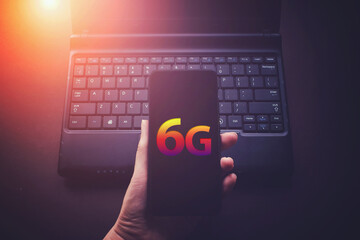 Woman hand holding smartphone and laptop computer with 6G connection. The concept of communication and internet on dark blue background