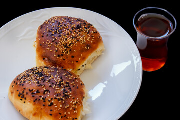 Close up Turkish pastry pogaca and tea on black background. Pastry food in white plate, breakfast snack.