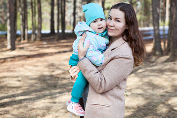 Fototapeta premium Portrait of mom with her little baby, female holding hands and embracing child in park