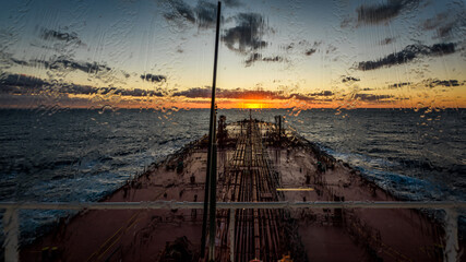 A super tanker is proceeding by ocean to sunset horizon