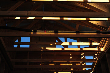 Wood framing and roof trusses illuminated by natural light during early residential construction,...