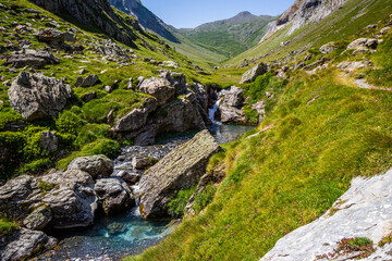 Beautiful turquoise blue waterfall surrounded by a green meadow with mountains in the background and a blue sky in springtime