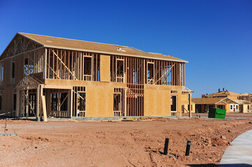 Two-story wood-frame house under construction in a developing neighborhood, illustrating residential homebuilding, suburban growth, and infrastructure expansion in planned housing communities