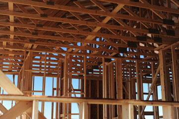 Framing detail of a wood-constructed residential building under development, highlighting roof trusses, vertical studs, and construction techniques used in suburban housing infrastructure