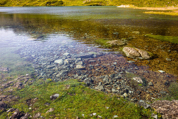 Crystal clear water of a lake surrounded by mountains, in a green meadow in summertime