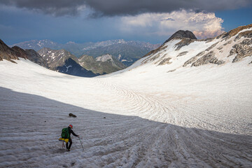 Climber crossing a glacier surrounded by mountains, with snow-capped mountains and a storm in the background