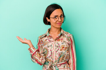 Young mixed race woman isolated on blue background doubting and shrugging shoulders in questioning...