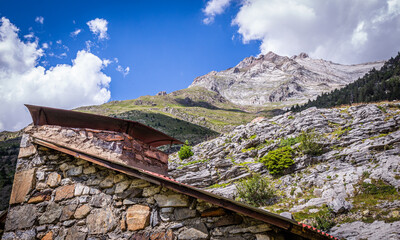 Beautiful view of a mountain top from a hut with a chimney in a green meadow in summertime