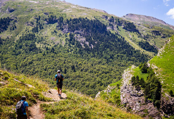Fototapeta na wymiar Hikers walking in summer through a beautiful green valley with trees and blue sky