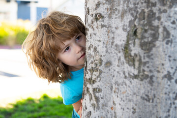 Kids games. Playing hide and seek. Peekaboo. Little boy hiding by tree.