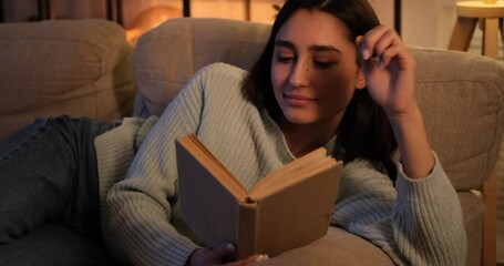 Woman reading book leaning on sofa at night