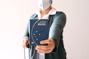 Woman using protective mask and holding a Brazilian passport. Travel and Covid-19 concept.