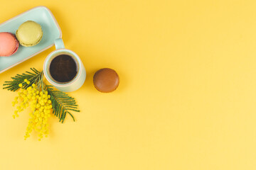 Fototapeta premium Coffee mug with cookies and mimosa flowers on yellow background. Copy space.