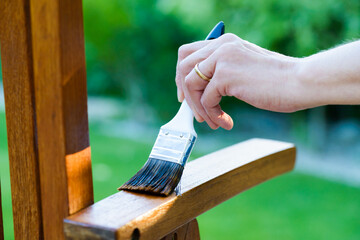 woman painting wooden exotic chair in the garden with a paintbrush - shallow depth of field