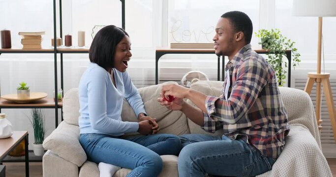 Man proposing woman with a ring and embracing on sofa at home