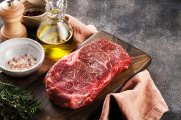 Fresh raw new-york steak on wooden board on grey background with salt, pepper and olive oil, top view, copy space.