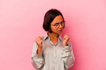 Young mixed race woman isolated on pink background showing fist to camera, aggressive facial expression.