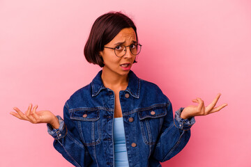 Young mixed race woman isolated on pink background doubting and shrugging shoulders in questioning...