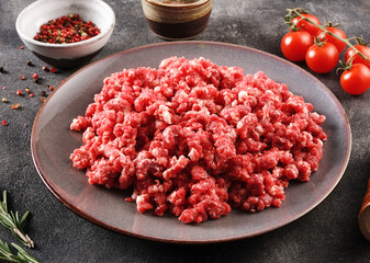 Homemade minced meat in a grey bowl over dark background or stone background with ingredients for making.