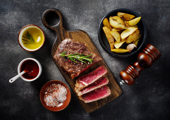 Sliced grilled meat steak New York Striploin with sauce and potato on wooden board on grey background.