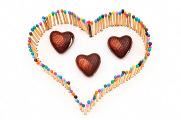 a heart shape made of multicolored matchsticks with heart-shaped candies in the middle