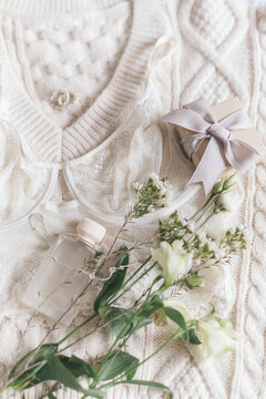 Stylish lingerie, perfume, modern jewelry and gift on sweater with spring flowers. Soft trendy image