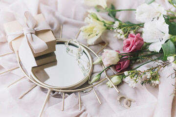 Stylish gift box, modern jewelry, spring bouquet on boho mirror on soft fabric. Happy Women's day