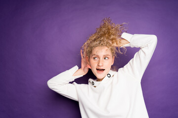  curly-haired woman depicts eavesdropping and holds her ear with her hand on a purple background