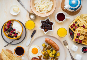 Family breakfast, set table for the whole family: full breakfast, whole grain granola with natural yoghurt and fresh berries, waffles with berries and whipped cream, rice porridge with butter.