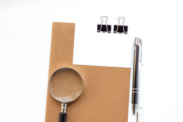 White office desk with magnifying glass, notepad with sticky note, pen with copy space. Accounting work space