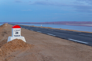 Milestone post on the Tozeur highway written in French and Arabic. Road passes through salt lake of...