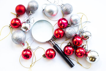 Magnifier glass on white table whith red and silver decoration ball. Business concept in new year. Search idea