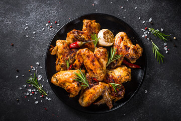 Grilled chicken wings with spices and rosemary at black table. Top view.