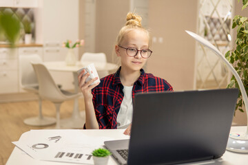 Blonde girl with glasses work on a laptop and rest at home. Home-school concept