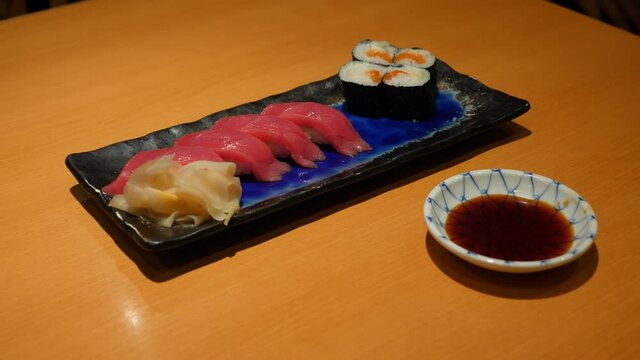Small plate of tuna nigiri and roll, man take piece by chopsticks and dip in soy sauce. Tasty fresh sea food served at common Japanese restaurant. Popular meal at Tokyo