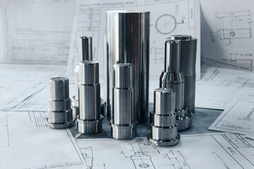 Metal products turned on a lathe lie on the drawings against the background of other drawings....