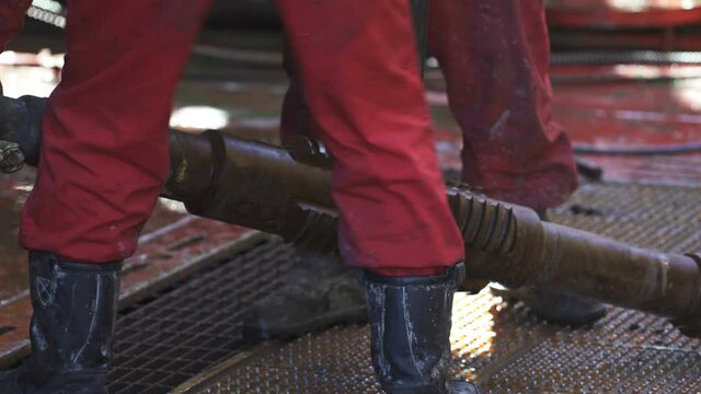 Drilling bit on a rope is carried away from the drilling site. Close-up. Engineers in red overalls and boots. Chisel is hanging on a rope