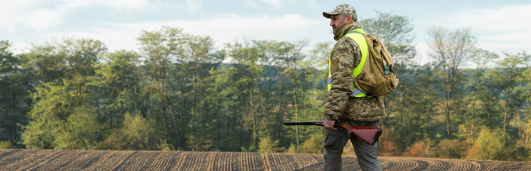A hunter with a gun in his hands in hunting clothes in the autumn forest in search of a trophy. A...