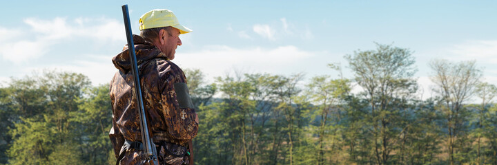 A hunter with a gun in his hands in hunting clothes in the autumn forest in search of a trophy. A man stands with weapons and hunting dogs tracking down the game.