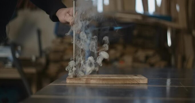 Carpenter puts hot stamp with red-hot tool to the wooden product with smoke in slow motion, marking the final product, 4k 60p Prores 422 HQ 10 bit