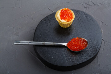 Bruschettes with butter and red caviar on a black round board.
