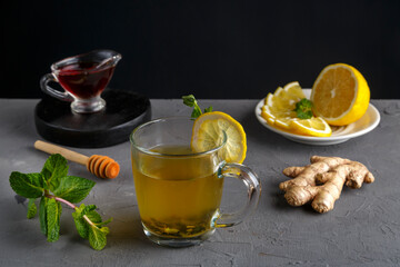 immune ginger drink with honey mint and lemon in a glass cup near ingredients on a concrete background.