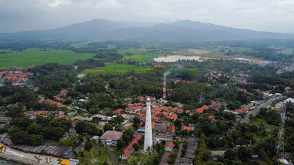 Fototapeta premium Aerial view of Lighthouse sea rock sunset landscape. Sunset lighthouse scene. At anyer beach with noise cloud and cityscape. 