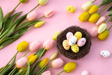 Obraz na płótnie Canvas Colorful easter quail eggs in nest and tulips on pink background with . Flat lay. Spring composition. Happy easter greeting card.