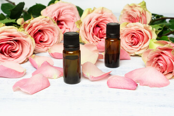 Bottles of rose essential oil with rose petals on the background of beautiful pink roses.