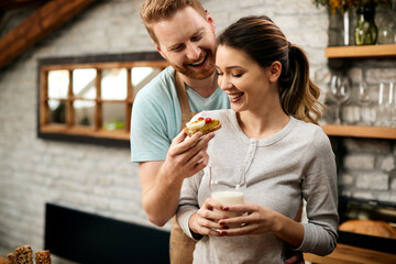 Happy man feeding his girlfriend in the morning in the kitchen.