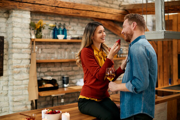 Romantic couple eating strawberries while drinking wine at home.