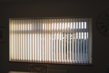 White vertical blinds on a window with bright sunlight behind them. there are slightly open. - 417479445