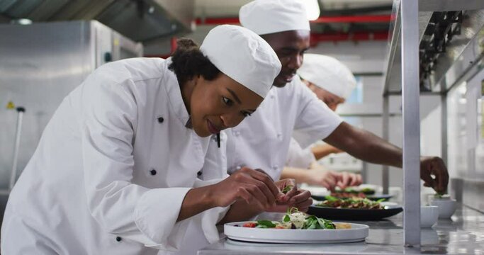 Diverse group of chefs garnishing dishes and similing in restaurant kitchen